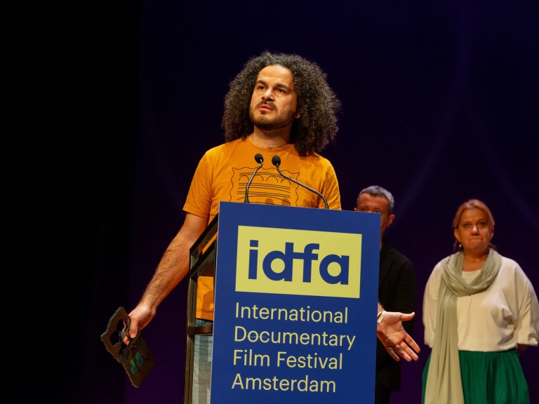 Mohamed Jabaly står ved en talerstol på IDFA med en pris i høyre hånd.