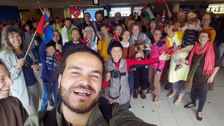 Regissør Mohamed Jabaly i forgrunnen foran gruppe med glade mennesker med forskjellige flagg.
