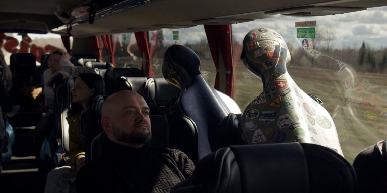 foto. mann sitter i buss og ser ut av vinduet med en stor instrumentkasse ved siden av seg
