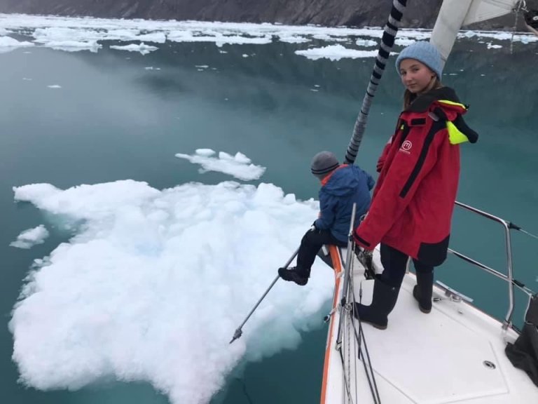 foto. to barn sitt i baugen på ein båt der den eine sjår ned på eit isflak i vatnet og den andre sjår mot kamera