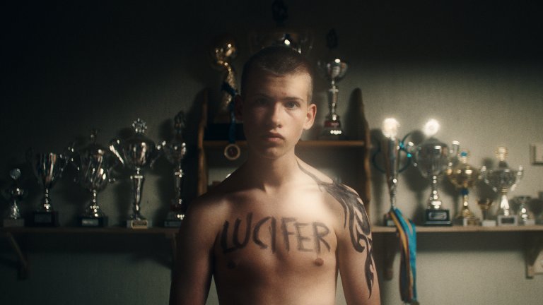 En gutt står i bar overkropp med ordet Lucifer skrevet på brystkassen.