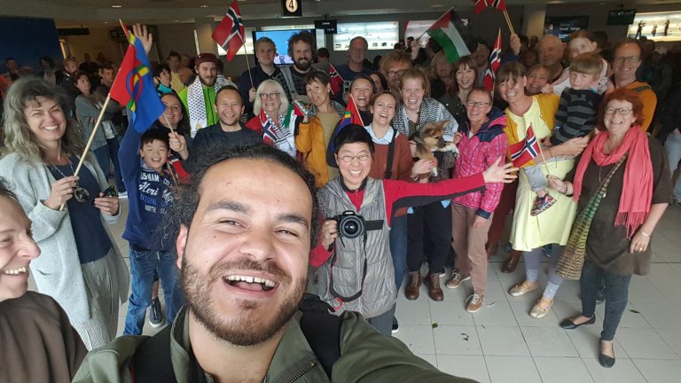 Foto: Stillbildet fra filmen er en selfie med regissør Mohamed Jabaly i forkant. Bak ham står en stor gruppe smilende mennesker. Flere av dem har norske flagg, og man kan også se et samisk og et palestinsk plagg.