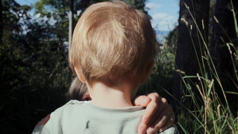 Foto: Bildet viser et barn bakfra. Viser bare hodet og en del av skuldrene. Vi kan skimte øyet til en annen person som holder en hånd på barnets høyre skulder.