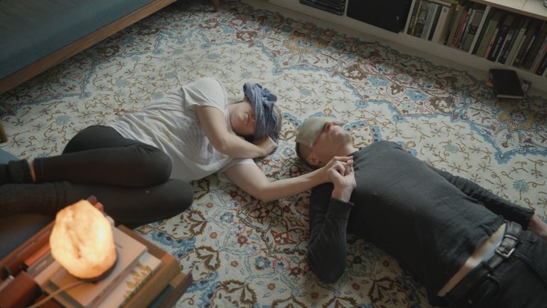 foto. to personer ligger ved siden av hverandre på et gulvteppe med bind for øynene og holder hverandre i hånden