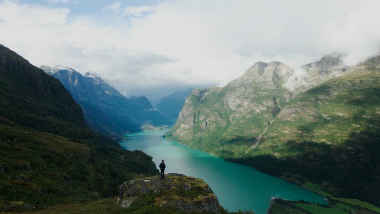 Bilde av norsk fjord med mann som står på stor stein og ser utover den.