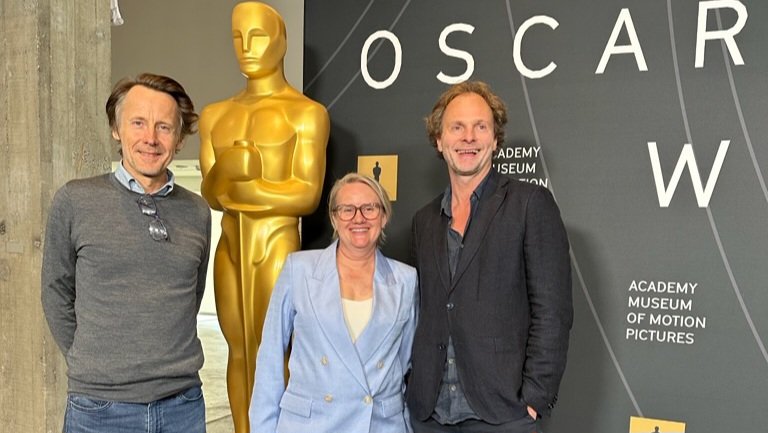 Foto: tre personer står foran en stor kopi av Oscar-statuetten, Nattrikken-regissør Eirik Tveiten og produsentene Heidi Arnesen og Gaute Lid Larssen