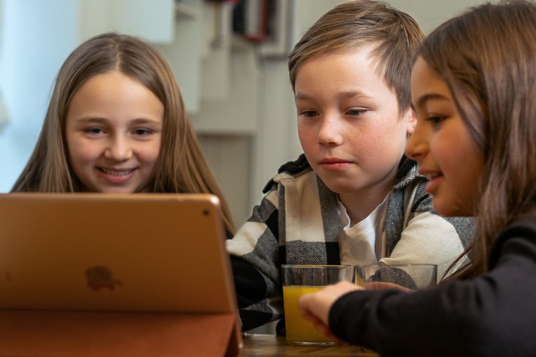 foto. tre barn sitter sammen foran en iPad skjerm
