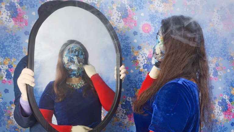 Kvinne kikker seg i speilet og ansiktet er dekket av et klede