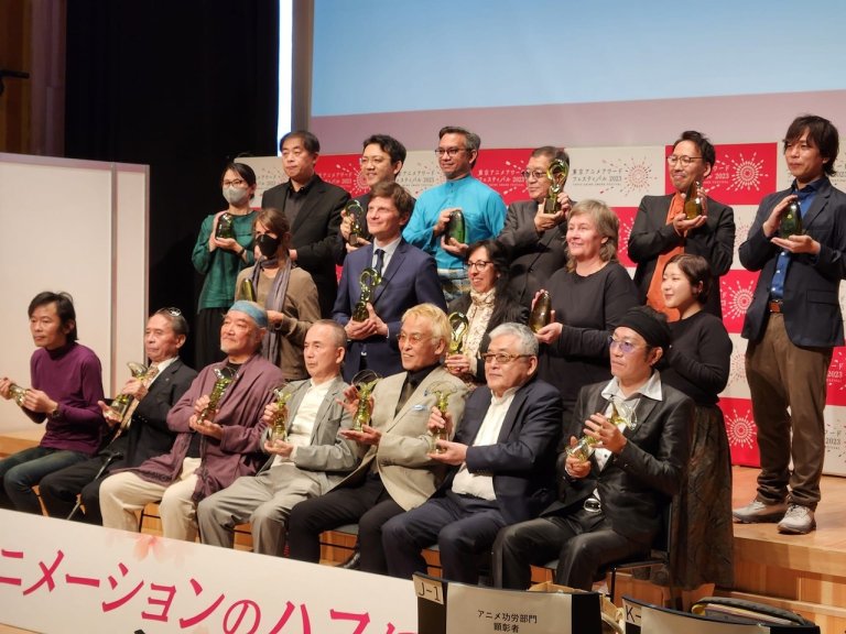 Foto. Sytten prisvinnere på et podium viser fram statuetter under Tokyo Anime Award Festival - Kajsa Næss står i andre rad