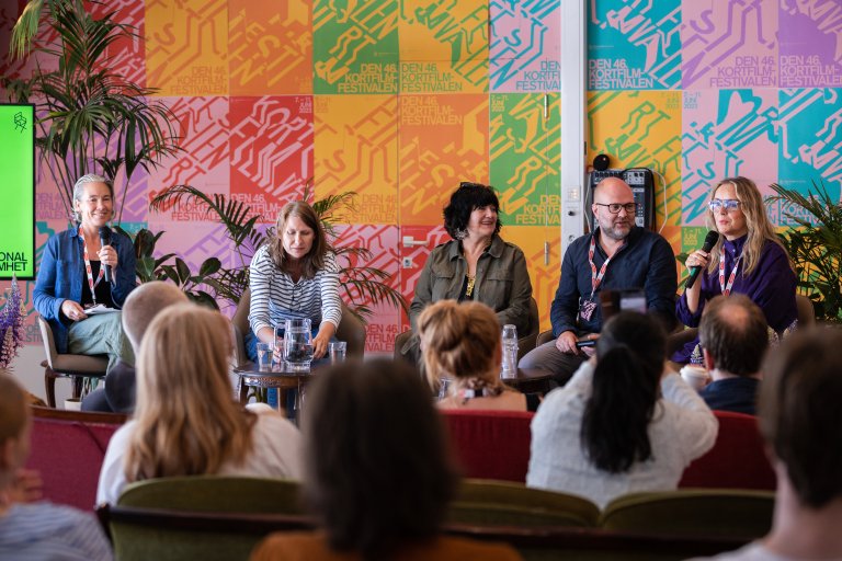 foto. fem personer sitter på scenen i paneldebatt foran festivalplakater med påskriften Den førtisjette Kortfilmfestivalen