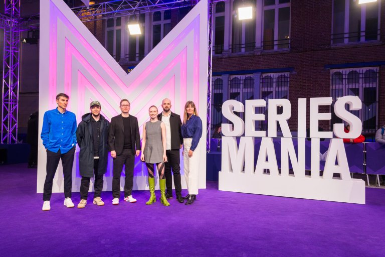 foto. bilde fra lilla løper med fem personer foran en stor logo av bokstaven m og et skilt med påskirften Series Mania