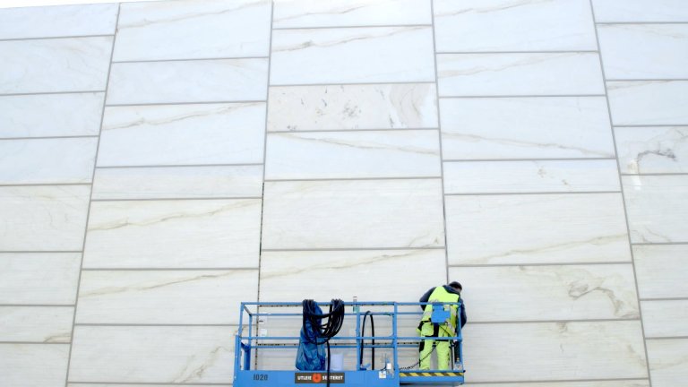 foto. eit stativ med ein mann i arbeidsklede på veg opp ein marmorvegg