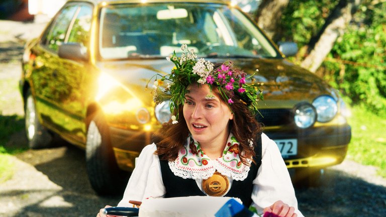 kvinne med blomster i håret foran gylden bil.