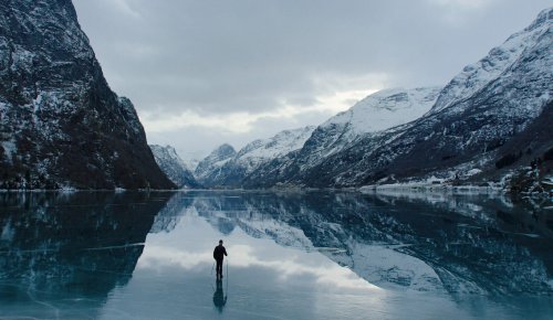 Foto. Islagt fjord og fjell og en mann går på isen